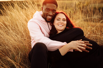 Adorable couple lay at the field, attractive husband gently hug adorable wife, overjoyed woman smiling, happy family spend time together, walking, weekends outdoors concept