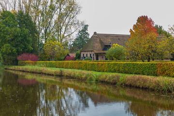 Fototapeta na wymiar Traditional Dutch farmhouse with thatched rood reflected in a canal during autumn in Drente, Netherlands