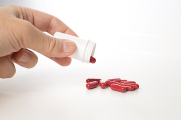 Red antibiotics capsule and plastic bottle between the fingers
