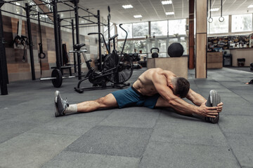 Fototapeta na wymiar Young muscular man practicing muscle stretching in modern health club