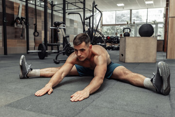 Fototapeta na wymiar Young muscular man practicing muscle stretching in modern health club