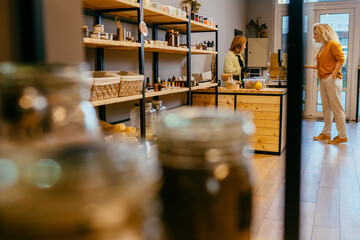 View of plastic free grocery store with blond female customer payment for purchases in zero waste...