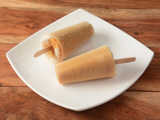 malai kulfi served in white plate over a rustic wooden background, selective focus
