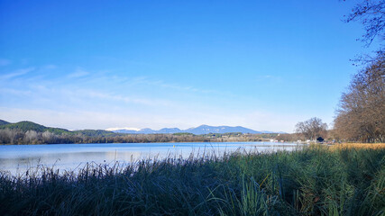 Photograph of a lake with tall grass in the foreground and mountains in the background