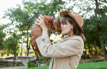 Portrait of a young fashion woman and a lovely dachshund puppy in a city park. Mistress and pet