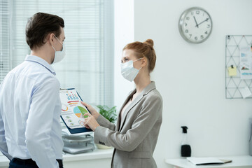 Obraz premium Two young elegant accountants in protective masks discussing financial diagram