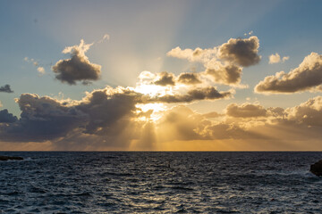 Naklejka na ściany i meble Sunsetting through clouds over the sea near Xlendi in Gozo.