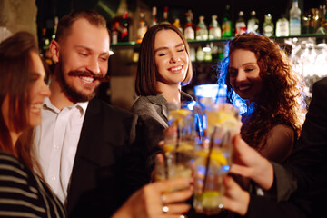Group of friends cheering and drinking cocktails together at the bar. Young people celebrating winter holiday together with coctails at a nightclub party. Youth, lifestyle, drink, birthday concept.
