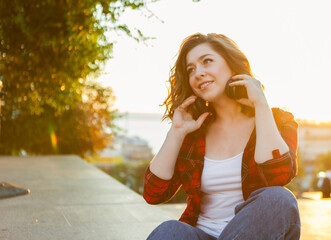 Portrait of an attractive smiling woman. Young hipster girl sitting on a concrete surface in the city at sunrise