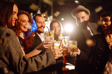Group of friends cheering and drinking cocktails together at the bar. Young people celebrating winter holiday together with coctails at a nightclub party. Youth, lifestyle, drink, birthday concept. 