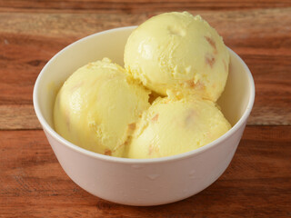 Butter scotch ice cream scoops served in a bowl over a rustic wooden table, selective focus
