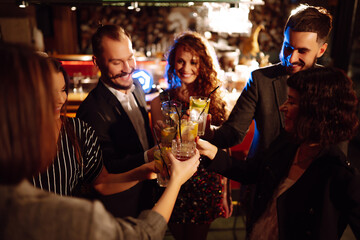 Group of friends cheering and drinking cocktails together at the bar. Young people celebrating winter holiday together with coctails at a nightclub party. Youth, lifestyle, drink, birthday concept.
