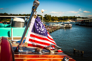 Nautical flag on back of teak wooden vintage speedboat in marina with docks and boats and retro...