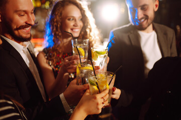 Group of friends cheering and drinking cocktails together at the bar. Young people celebrating winter holiday together with coctails at a nightclub party. Youth, lifestyle, drink, birthday concept.
