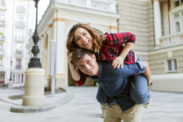 Young couple having fun outdoors. Handsome man giving his girlfriend piggy back ride. Enjoying...