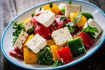 Fresh Greek salad - feta cheese, tomatoes, cucumber, three color pepper, black olives and onion on wooden table
