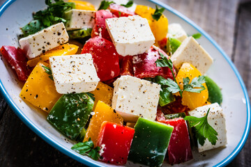 Fresh Greek salad - feta cheese, tomatoes, cucumber, three color pepper, black olives and onion on wooden table
