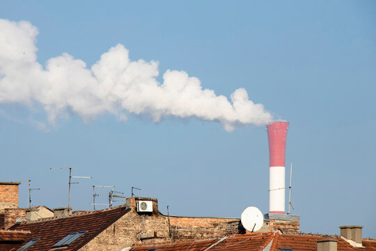 Heating and power station chimney smokestack with smoke, with rooftops of old houses and anthenas