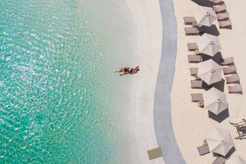 Aerial view of a couple lying alone on a beach and enjoying the summer sun next to the turquoise sea