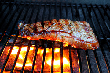 Steak on a grill, lighted from below, glowing orange, brown grill lines from cooked area on top.