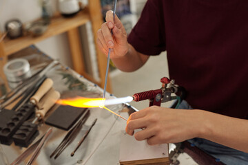 Hands of young contemporary female artisan holding workpieces over fire
