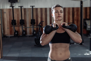 Muscular woman athlete holding heavy kettlebells. Functional, cross training in a modern gym.