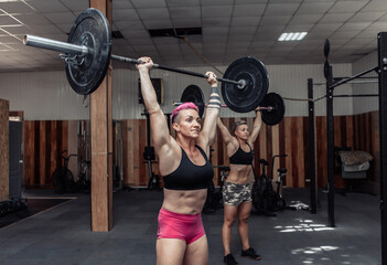 Fototapeta na wymiar Strong women bodybuilder doing overhead with heavy barbell in modern cross gym. Functional training class. Bodybuilding and Fitness