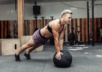 Fototapeta na wymiar Muscular athletic woman push ups with medicine balls in a modern gym. Cross fit, functional training