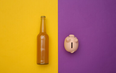 Alcohol costs. Beer bottle and piggy bank on a purple-yellow background. Top view