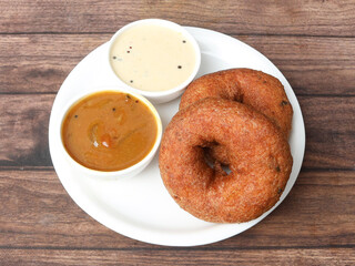 Indian fried snack Medu Vada with sambar and coconut chutney in plate on rustic wooden background, savoury fried snack of Kerala, Tamil Nadu and South India. selective focus