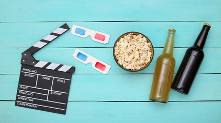 Movie time. Movie clapperboard, 3d glasses, bottles of beer, popcorn on blue wooden background. Top view