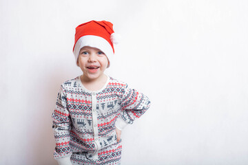 The boy in the Santa hat is laughing . Boy on a white background. Red cap. Reindeer pajamas.