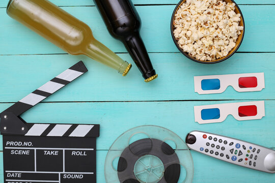 Movie time. Movie clapperboard, tv remote, film reel, 3d glasses, bottles of beer, popcorn on blue background. Top view