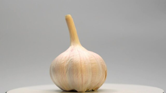 Head of garlic close-up against a white background. The garlic rotates slowly. 