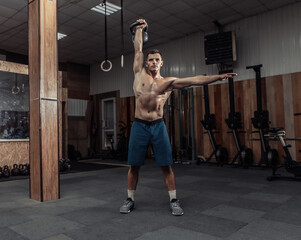 Obraz na płótnie Canvas Muscular powerful man exercising with heavy kettlebell in cross fit gym. Functional training with free weights