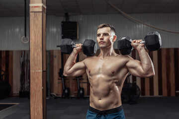 Fototapeta na wymiar Powerful athletic man training shoulder muscles with heavy dumbbells in the gym