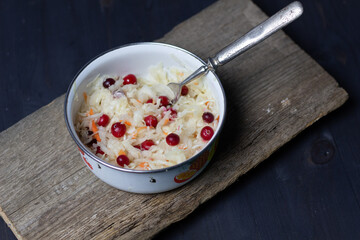 Fermented cabbage with cranberries in white bowl with fork on rustic wooden background