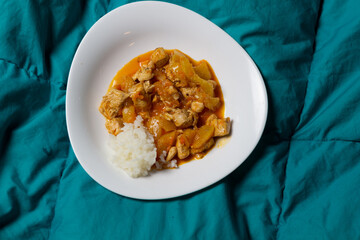 rice with spicy curry chicken and vegetables in white plate on green textile background