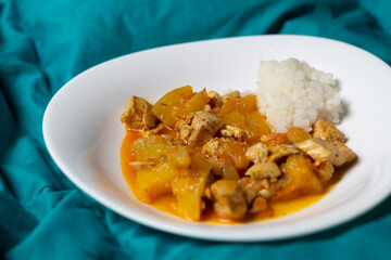 rice with curry chicken and squash in white plate on green textile background