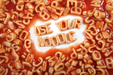 The words ‘use your noodle’ written in alphabetti spaghetti, orange pasta shaped letters.
