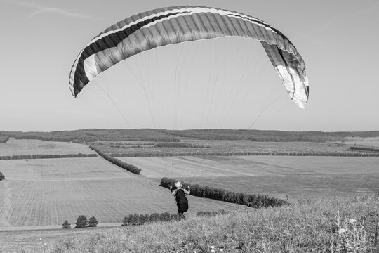 Beautiful view of a pilot with paraplan going to start flying over the fields in the summer morning. Black and white photo