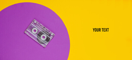 Audio cassette on yellow background with purple circle and space for your text. Studio fashion shot. 80s, pop culture. Top view.
