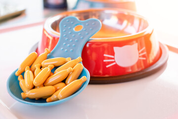 Animal food supplements concept. Bowl and spoon full of tablets, pills, softgel, capsule, treats....