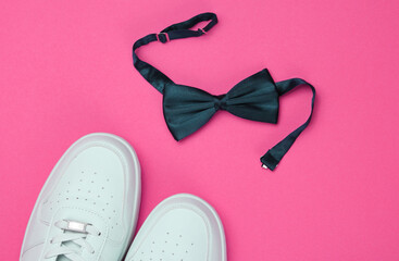 Stylish white sneaker and bow-tie on pink paper background. Minimalistic fashion concept. Top view