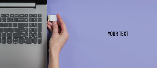 Female hand inserts SD memory card into laptop on purple background with space for your text. Top...