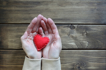 I love you recognition. Female hands and a red felt heart with white stitches on a vintage wood...