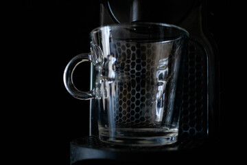 Transparent glass cup in an espresso machine. Concept drinks, work, rest. Dark background