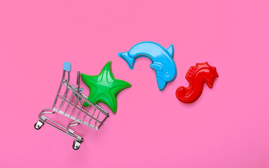 Shopping trolley with toy forms for the sand (beach toys) on pink background. Top view