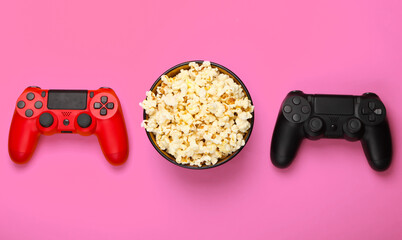 Two gamepads and a bowl of popcorn on pink background. Gaming, leisure and entertainment concept. Top view