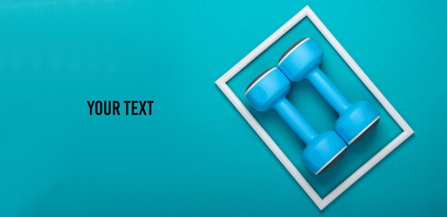 Plastic dumbbell on blue background with white frame and space for your text. Fashion shot. Creative flat lay. Top view. Minimalism
